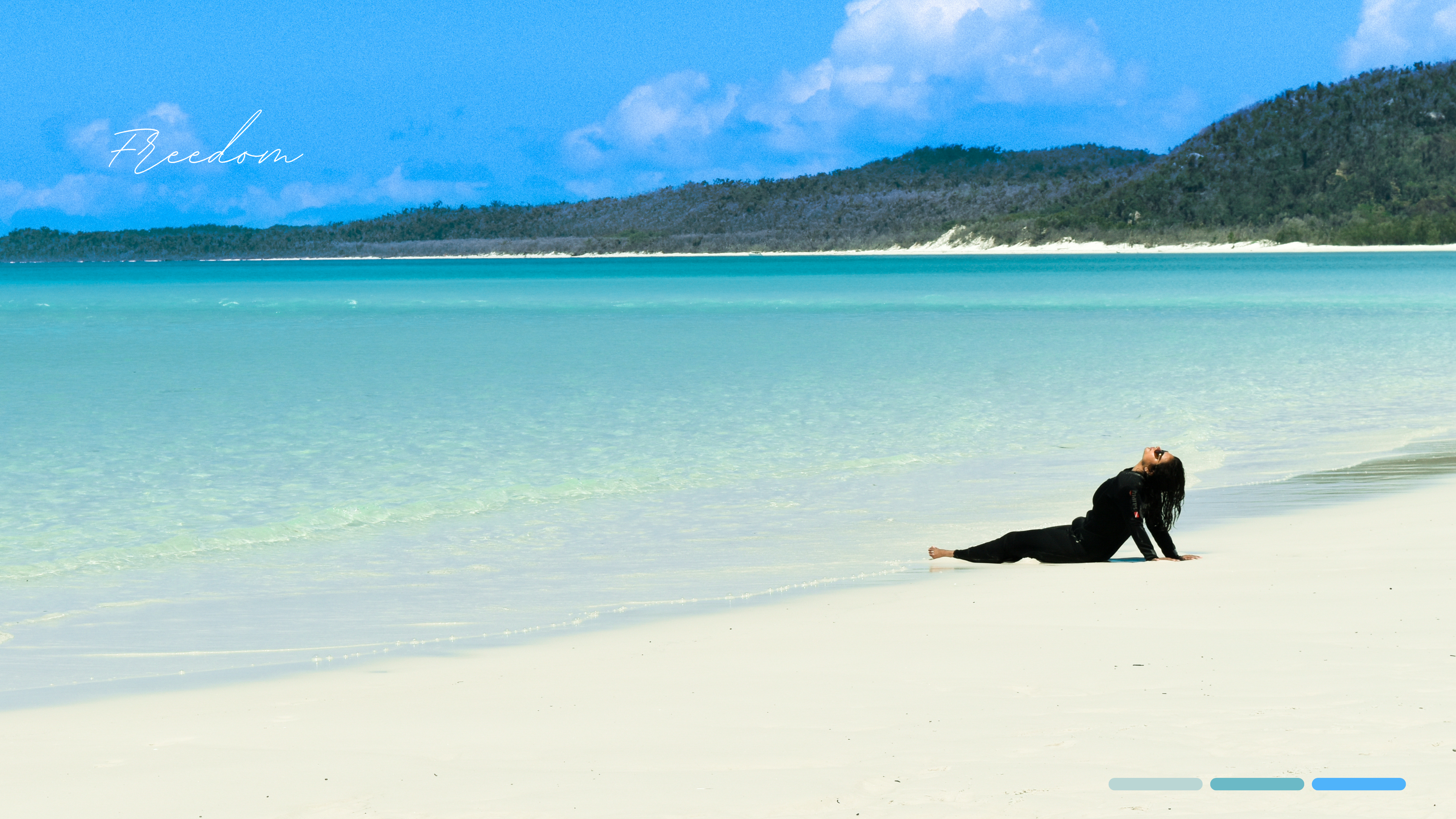 Woman sitting on a white sand beach with turquoise water and green hills